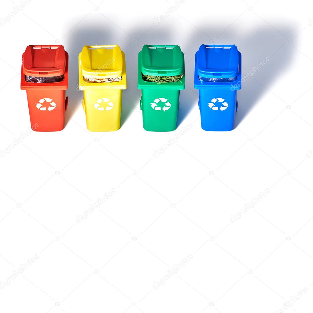 Four color coded recycle bins, isometric projection on geometric rainbow paper background with copy-space. Recycling sign on the bins - red, blue, yellow and green on white. Waste separation concept.