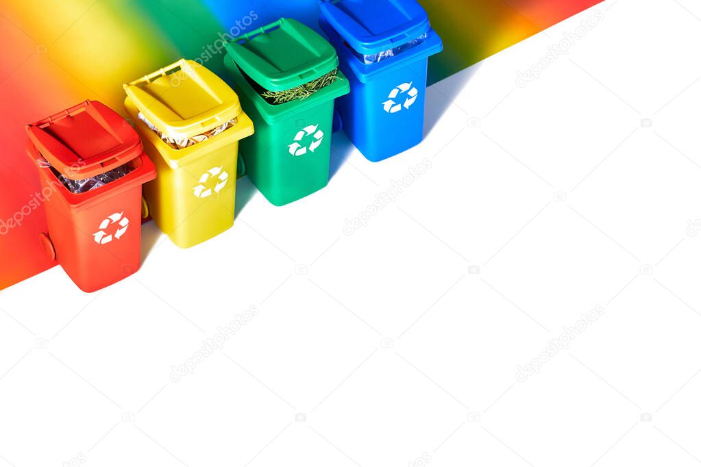 Four color coded recycle bins, isometric projection on geometric rainbow paper background with copy-space. Recycling sign on the bins - red,  blue, yellow and green. Waste separation concept.