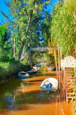 Lush vegetation, motor boats and old wooden pier. Tigra delta in Argentina, canals and river system of the Parana Delta North from the capital, Buenos Aires. clipart
