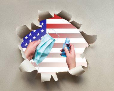 Yüz maskeli eller ve dezenfeksiyon jeli kağıt delikte Amerikan bayrağıyla. Covid-19 Coronavirus hijyen tedbirleri, yeni koronavirüsün kamu sağlığını tehdit etmesini önlemek için zatürreeye yol açtı..