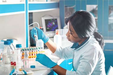 Laboratuvar önlüğü ve nitril eldivenli Afrikalı bilim adamı veya lisansüstü öğrencisi modern test laboratuvarında RT-PCR testi yapıyor.