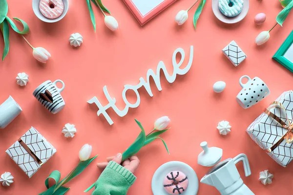 ホーム という言葉 春のオブジェクトやシンボルと大胆なピンクの背景に創造的なトップビュー 手は白いチューリップを持っています 幾何学的配置 ホーム コーヒーメーカー エスプレッソカップ ドーナツ — ストック写真