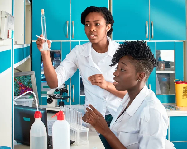 Two female African medical students or young graduates in research or medical test laboratory performing various testing on samples. Microscopic analysis biopsy, pcr nucleic acid test for coronavirus.