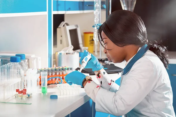 African scientist or graduate student in lab coat and protective wear performs RT-PCR testing in modern test laboratory