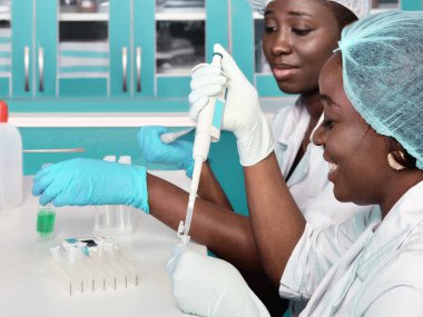 Laboratuvar önlüğü ve eldiven giyen iki Afrikalı bilim adamı, teknik asistan ya da mezun test laboratuarı ya da tıbbi tesiste hasta örneklerini PCR testine tabi tutuyorlar. Salgınla mücadele için RT-QPCR testi devam ediyor.