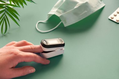 Nabız oksimetresi taşınabilir dijital cihaz kişinin oksijen doygunluğunu ölçmek için. Oksijendeki azalma acil olarak hastaneye yatırılması gereken bir zatürre belirtisidir. Yeşil nane arkaplanı.