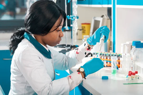 African scientist or graduate student in lab coat and protective wear performs PCR testing of patient samples in modern test laboratory. Developing pcr kits to diagnose Covid-19 patients.