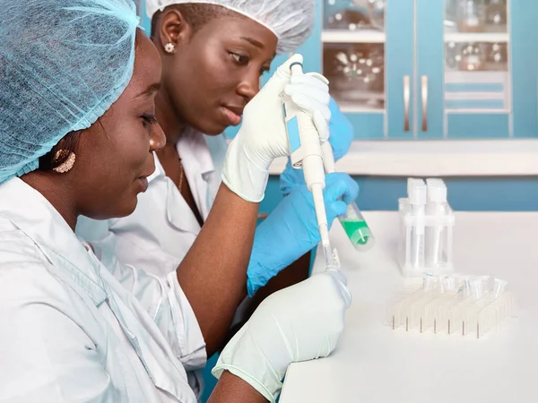 Two African scientists, technical assistants or graduates in lab coats and gloves perform PCR testing of patient samples in test laboratory or medical lab. Smiling energetic professionals work hard.