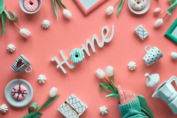 春のオブジェクトとシンボルで活気のあるピンクの背景に家のメッセージ 創造的なフラットレイアウトを維持します 手は白いチューリップを保持 幾何学的な装飾 ホーム コーヒーメーカー エスプレッソカップ ドーナツ — ストック写真