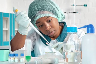 Beyaz önlüklü, koruyucu şapkalı ve eldivenli Afrikalı bilim adamı, teknik asistan veya tıbbi teknisyen modern test laboratuvarında SARS-CoV-2 virüsü için PCR testini optimize ediyor. Araştırma tesisi..