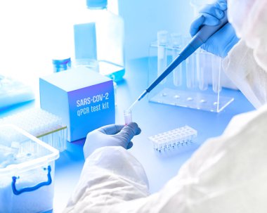 SARS-COV-2 PCR tanı kiti. Koruyucu giysi, maske ve gözlük giyen epidemiyoloji uzmanı hasta örneklerindeki virüsü tespit etmek için reaksiyonu karıştırıyor. PCR 2019-nCoV virüsünün Covid-19 pnömonisine neden olduğunu tespit etti.