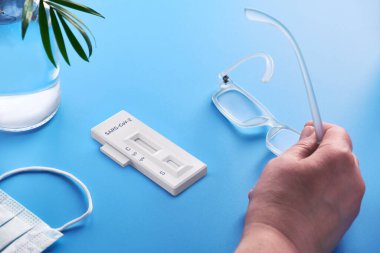 İgm ve IgG 'nin Corona virüsü SARS-CoV-2' yi geliştirerek Covid-19 zatürreeye neden olan özel antikorların tespiti için hızlı COVID-19 testi. El ele tutuşan okuma gözlükleri, mavi arka planda palmiye bitkisi testi.