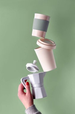 Yeşil naneli arka planda kadın eliyle tutulan sıfır atık kahve piramidi. Seramik espresso sobası kahve makinesi ve çevre dostu yeniden kullanılabilir kapaklı bambu kahve kupası.