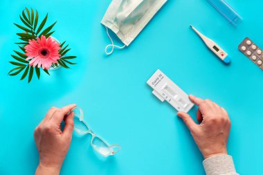 Covid-19 'a neden olan koronavirüsü geliştirmek için IgM ve IgG antikorlarının tespiti için hızlı COVID-19 testi. Test ve gözlüklü eller. Yüz maskesi, termometre ve haplar, turkuaz arka plan..