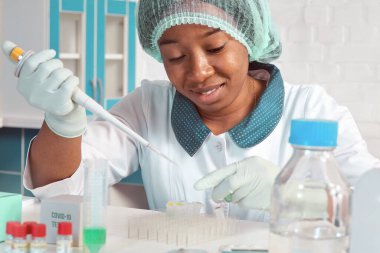 Laboratuvar önlüğü, koruyucu şapka ve eldiven giyen Afrikalı bayan teknik asistan SARS-CoV-2 virüsü test etmek için tıbbi test tesisinde PCR testi yapıyor. Yeni koronavirüs için PCR testlerinde sorun..