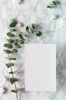 Taze okaliptüs dalları ve beyaz siyah ıvır zıvırlarla dolu bir Noel çerçevesi. Yıldızlı mücevherler. Düz konum, beyaz mermer zemin üzerinde üst görünüm, metin boşluğu, kopyalama alanı, metin için yer.
