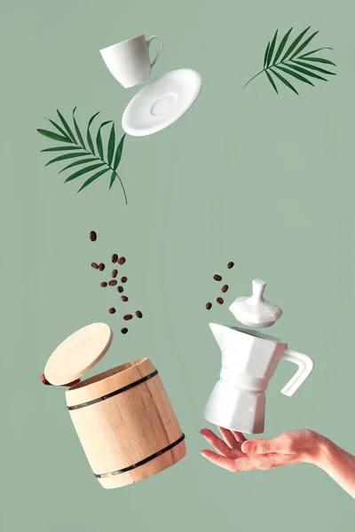 飘飘欲仙的飘浮咖啡豆 浓缩咖啡杯 木桶盖 陶瓷炉咖啡机在女人的手上保持平衡 绿色薄荷现代背景棕榈叶 — 图库照片
