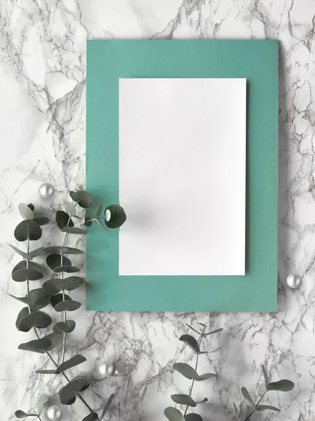 Christmas frame with fresh eucalyptus twigs and white black trinkets, baubles with stars. Flat lay, top view on white marble background, blank paper page with text space, copy-space.
