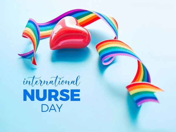 International nurse day thank you card. Rainbow ribbon and red ceramic heart on light blue mint background. Symbols of public support for nurses and medical personnel.