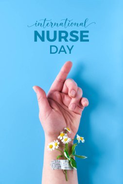 International nurse day. Hand of mature woman with chamomile flower bouquet attached with medical aid patch. Creative modern flat lay, top view on blue background. clipart