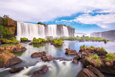 Arjantin 'de Iguazu şelaleleri. Sis ve bulutlarla dolu birçok görkemli ve güçlü su çağlayanlarının panoramik görüntüsü. Iguazu Vadisi 'nin panoramik görüntüsü. Sakin sularda otlar ve taşlar var..