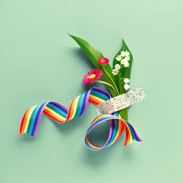 Thank you doctors and nurses! Rainbow ribbon and bouquet of red primrose and lily of the valley flowers attached with medical aid patch. Creative panoramic flat lay, green mint background, copy-space.