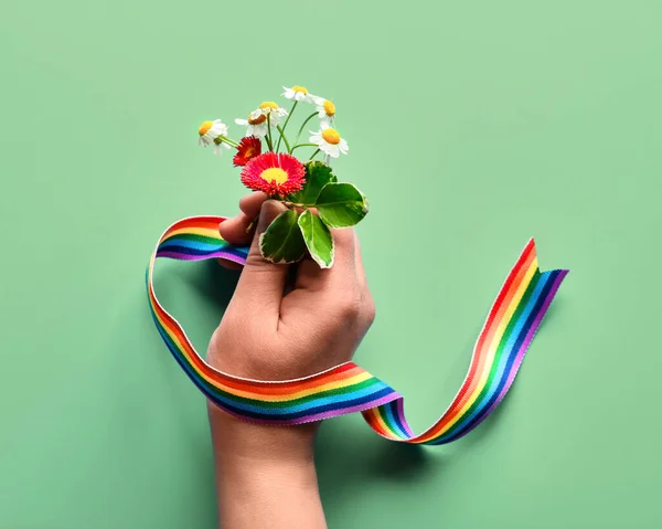 Thank you doctors and nurses! Rainbow text, ribbon in hand of woman with chamomile and primrose flowers, simple bouquet. Creative flat lay, top view on light green mint background.