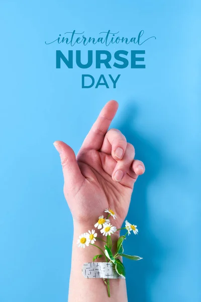 International nurse day. Hand of mature woman with chamomile flower bouquet attached with medical aid patch. Creative modern flat lay, top view on blue background.