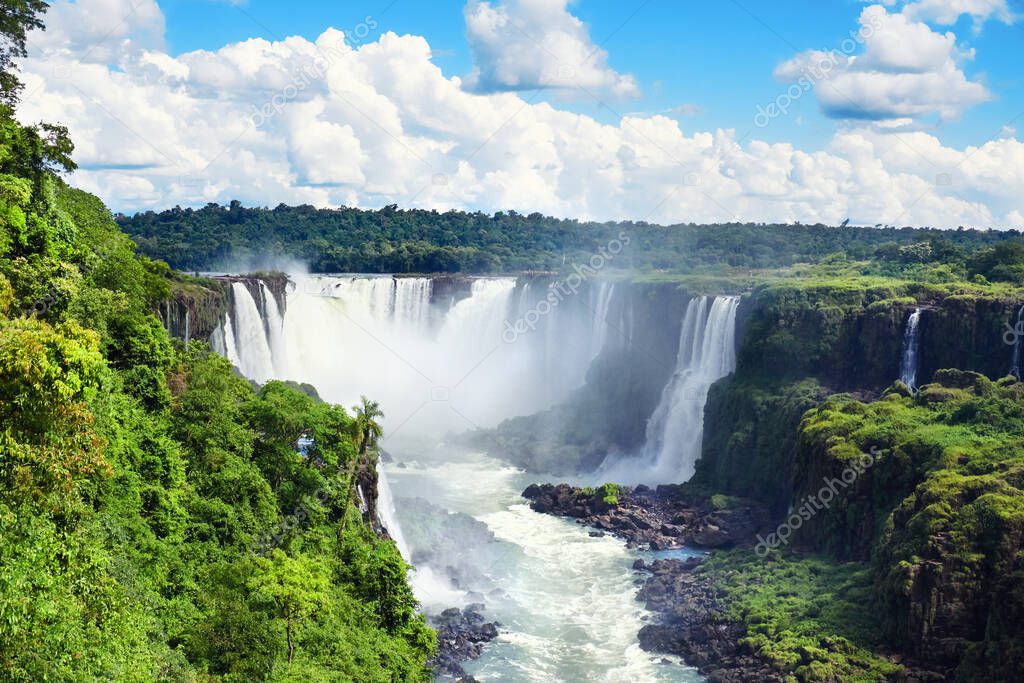 Iguazu waterfalls in Argentina, view from Devil's Mouth. Panoramic view of many majestic powerful water cascades with mist. Panoramic image with blue sky and clouds.