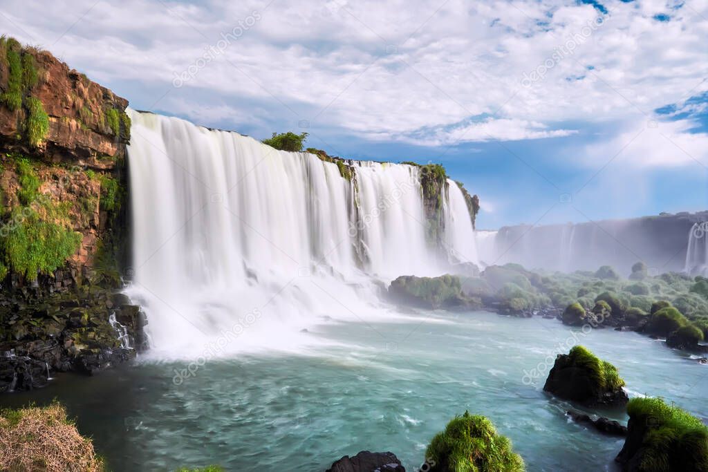 Iguazu waterfalls in Argentina, view from Devil's Mouth. Panoramic view of many majestic powerful water cascades with mist. Side view of the wide powerful waterfall. Turquoise water and stones.