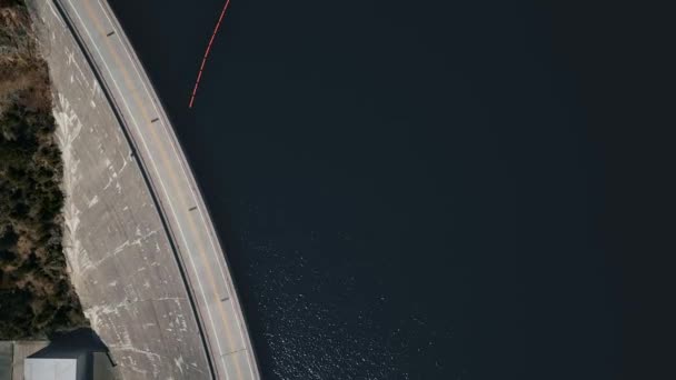 Overhead drone shot over a road on a dam in front of a river and a passing red car Hungry Horse Dam, Flathead River, Montana, EUA — Vídeo de Stock