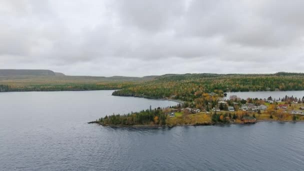 La cámara del dron se aleja de la orilla con un denso bosque otoñal y asentamiento junto al lago Lake Superior, Great Lakes, Ontario, Canadá — Vídeos de Stock