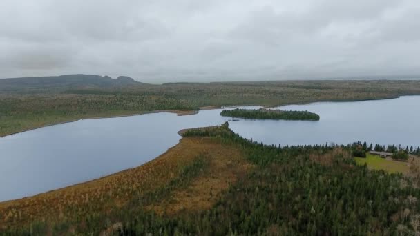Luftaufnahmen eines Sees zwischen bewaldeten Ufern, einem Häuschen und Bergen am Horizont an einem bewölkten Tag Marie Louise Lake, Ontario, Kanada — Stockvideo