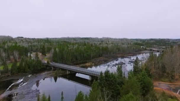 Drone camera approaches a bridge between the shores with a road and an autumn forest Kaministiquia River, Ontario, Canada — Stock Video