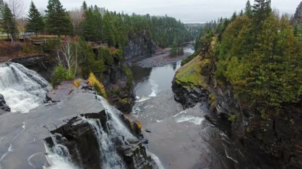 Drone πετά πάνω από έναν καταρράκτη, γκρεμούς, φθινοπωρινά δάση και ρηχά νερά στο φαράγγι σε μια συννεφιασμένη μέρα Kaministiquia River, Kakabeka Falls, Οντάριο, Καναδάς — Αρχείο Βίντεο