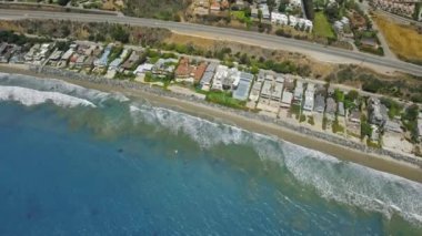 Deniz kıyısındaki evlerle mavi okyanusun hava görüntüleri, geçen arabaların bulunduğu bir yol Malibu, California, ABD 'de. 