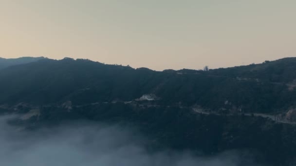 Drone camera shoots mountains with a dense forest and a winding road in fog from a birds eye view above the clouds Malibu Canyon, Calabasas, California, USA — Stock Video