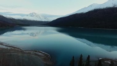 İnsansız hava aracı, ABD 'nin Alaska eyaletindeki Eklutna Gölü' ndeki sakin bir nehre yansıyan karlı dağlara yaklaşıyor.