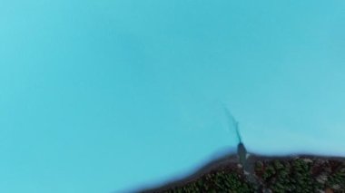 Amerika 'nın Alaska eyaletindeki Eklutna Gölü kıyısında yoğun bir ormanla birlikte açık mavi göl suyunun insansız hava aracı görüntüsü.