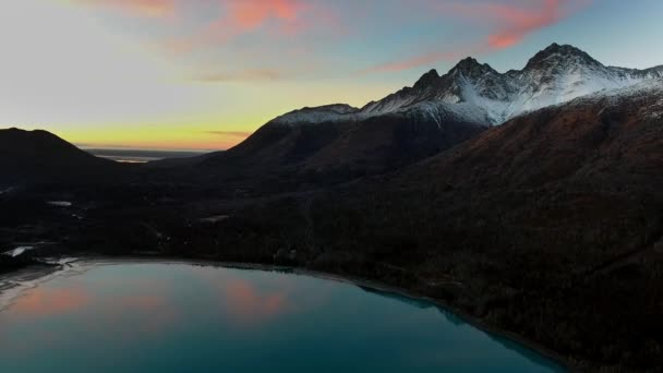 드론은 눈덮인 정상, 발에 있는 숲, 미국 알래스카의에 클루 트나 호수에 있는 거울 호수와 일몰 이 있는 산으로 서서히 접근하고 있다 — 비디오
