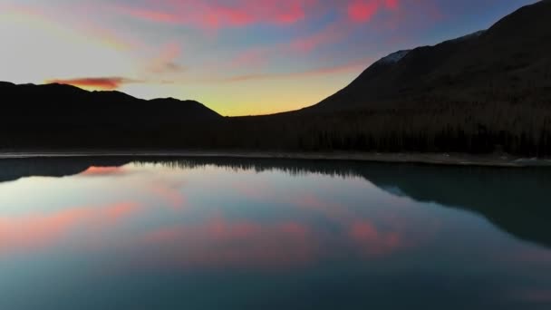 Беспилотник фиксирует отражение пурпурных облаков в озере возле горы на закате на озере Эклутна, Аляска, США — стоковое видео