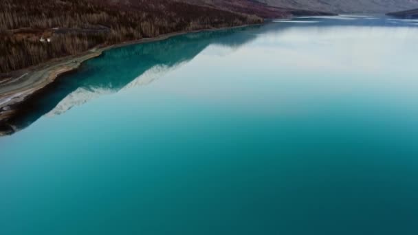 Tiro aéreo de água azul para montanhas nevadas com floresta densa em um dia claro no Lago Eklutna, Alasca, EUA — Vídeo de Stock