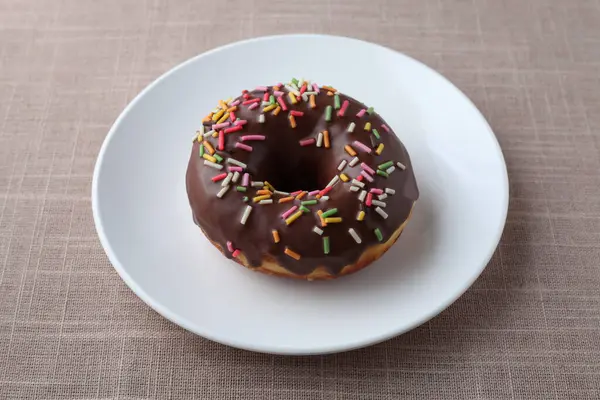 Chocolate frosted doughnut on plate on table — Stock Photo, Image