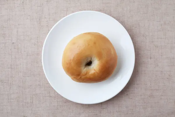 Plain bagel bread on plate isolated on table cloth — ストック写真
