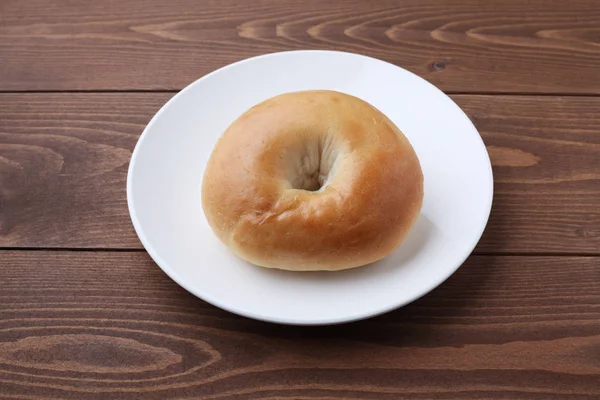 Pan de bagel liso en plato aislado en mesa de madera —  Fotos de Stock