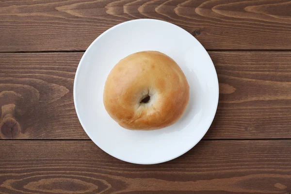 Plain bagel bread on plate isolated on wooden table — ストック写真