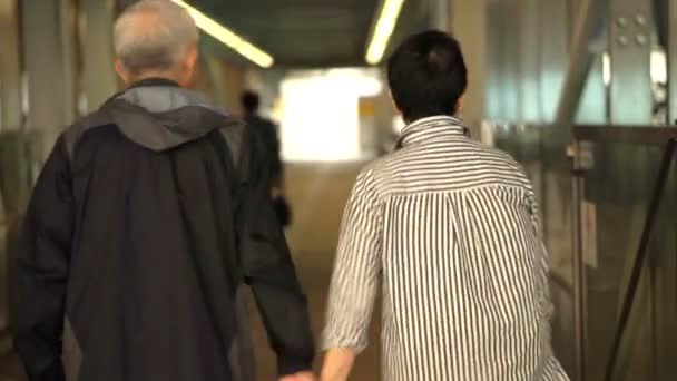 Ασιατικό ανώτερα συνταξιούχο ζευγάρι περπάτημα πιασμένοι χέρι χέρι κατά μήκος της διάδρομος κάλυψη από το σιδηροδρομικό σταθμό συγκυριαρχία — Αρχείο Βίντεο