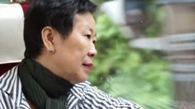 Trende oturan ve pencereden bakan kıdemli Asyalı kadın. Düşünme ve emeklilik gezisi sırasında manzarayı