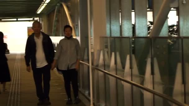 Asiatique retraité couple marche tenant la main le long de la passerelle de couverture de la gare à la copropriété — Video