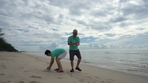 Asian elderly couple collecting shells on the beach — Stock Video
